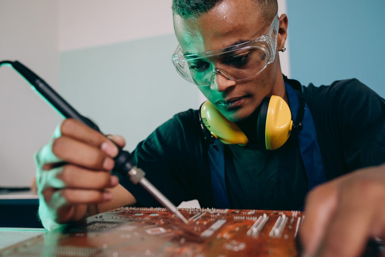 Young male engineer working on circuit board soldering with precision and focus.
