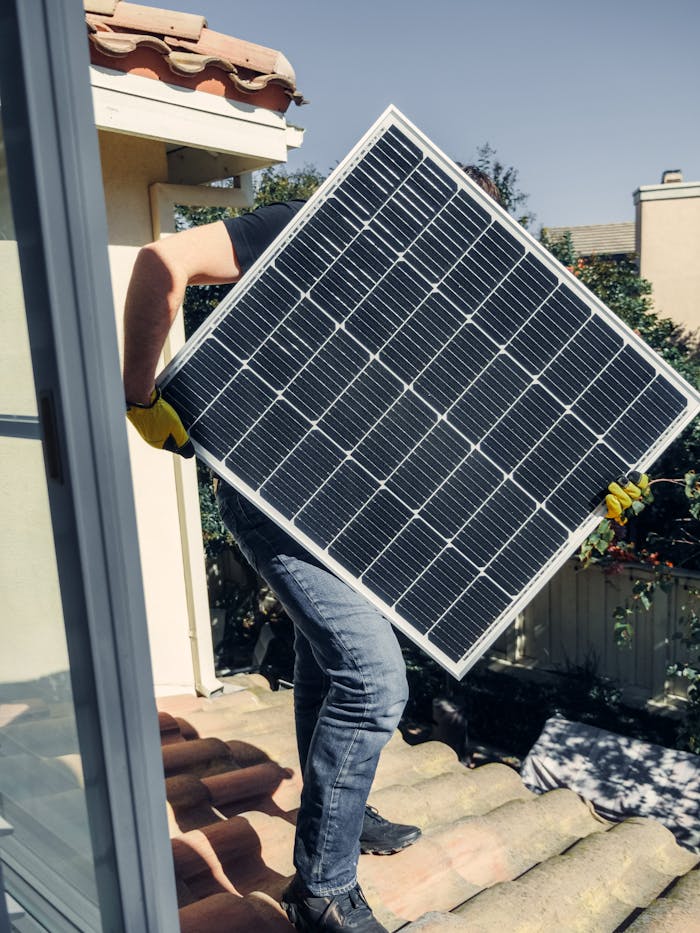 A worker carrying a solar panel for installation on a sunlit rooftop, showcasing clean energy.